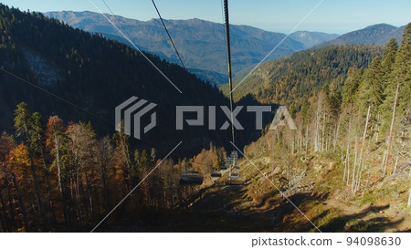 Scenic view from cable car cabin moving down among the autumn colored trees in magnificent caucasus mountains. downhill on cable road among forested mountain range. 94098630