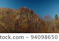 Forested rock of caucasian mountain range painted in autumn colours. there is clear sky and sunlight over trees coloured in bright yellow, red and green colours. 94098650