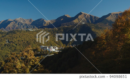 Amazing aerial view from funicular cabin on rosa khutor village. the rays of the sun fall on the beautiful caucasus mountains covered with autumn colorful trees. 94098651