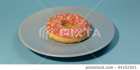 Pink doughnut or donut with colored sprinkles on a blue background. Bitten off American bagel. Pink doughnut or donut with colored sprinkles on a blue background. Bitten off American bagel. 94102801