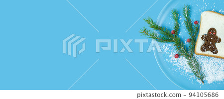 Christmas creative food. Blue plate with toast, gingerbread man, spruce branch, frozen berries and coconut snow on a blue background. Background for New Year's menu. Flat lay, banner, copy space. 94105686