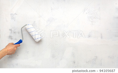 Hand with paint roller on background of empty concrete white wall. Priming the walls. Repair, redecoration, wall painting, painting, interior renovation, moving. Copy space. 94105687