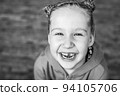 Black and white close-up portrait of a laughing little girl with a missing front tooth. Cheerful child. Real sincere emotions, happiness, childhood. 94105706