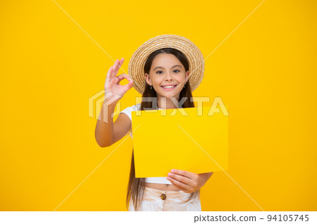happy teen girl hold empty advertisement paper with copy space on yellow background. ok 94105745