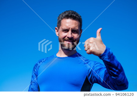 success at any cost. handsome athlete show thumb up. confident man on stadium. fitness gym outdoor. muscular athletic guy training. sport success. male fitness fashion. sportsman on sky background 94106120