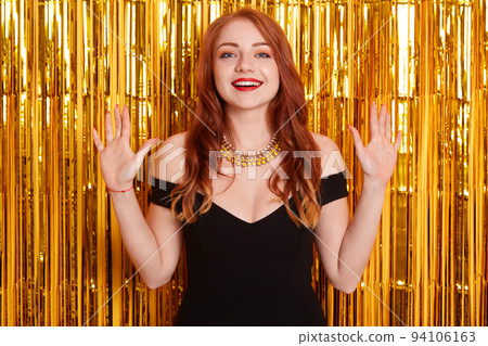 Beautiful excited woman with beautiful red hair at celebration party, birthday or New Year eve celebrating, happy girl in dress raising hands up, looks excited. 94106163