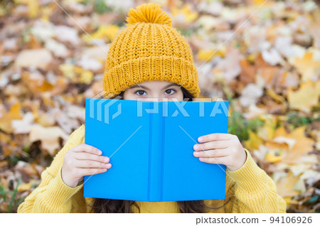 There is no companion more steadfast than book. Little child cover face with book autumn leaves. Knowledge day. School library. Reading education. Literature lesson. Imagination and fantasy 94106926