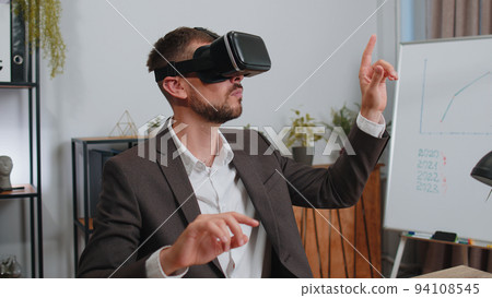 Businessman working using virtual reality futuristic technology VR app headset helmet at home office 94108545