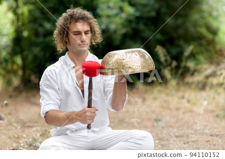 A man playing on a singing tibetian bowl for relaxation and meditation. Buddhist healing practices and sound therapy 94110152