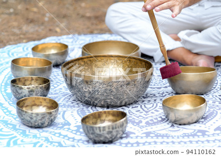 Close-up of man hands playing on a singing tibetian bowl with sticks. Sound healing music instruments for meditation 94110162