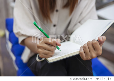 The girl's hand holding a pen is writing down something on a notebook. 94114017