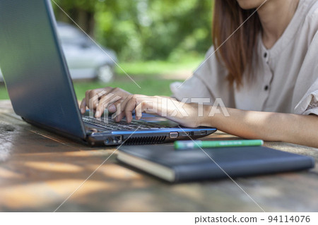 Hands pressed on the laptop keyboard on the desk outdoors in the shady atmosphere suitable for working. 94114076