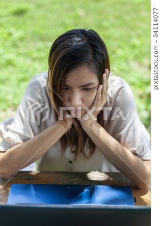 Asian woman gesturing while staring at something on a laptop screen 94114077