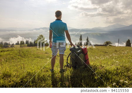Hiker with a backpack standing in mountains Hiker with a backpack standing in mountains 94115550