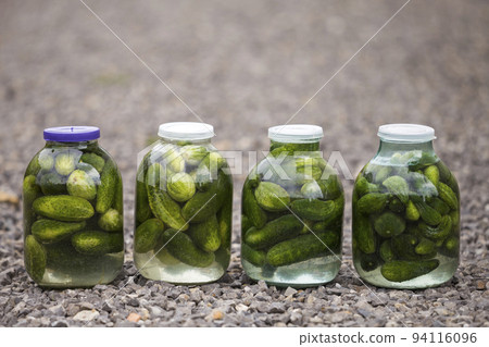 Big glass jars with green fresh pickles cucumbers salted in marinade on abstract blurred background. 94116096