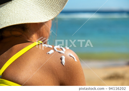 Back view of young woman tanning at the beach with sunscreen cream in sun shape on her shoulder. UV sunburn protection and sunblock skincare concept Back view of young woman tanning at the beach with sunscreen cream in sun shape on her shoulder. UV sunburn protection and sunblock skincare concept 94116202