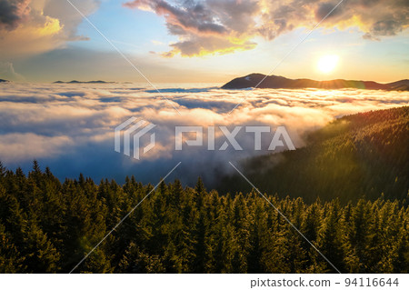 Aerial view of vibrant sunrise over mountain hills covered with evergreen spruce forest in autumn. Aerial view of vibrant sunrise over mountain hills covered with evergreen spruce forest in autumn. 94116644