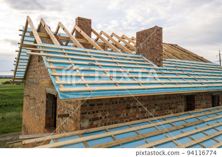 Aerial view of a brick house with wooden roof frame under construction. 94116774