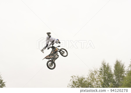 Freestyle motocross. Biker rider doing a jumpin the air. Perfoming acrobatic stunt flying. Fmx motocycles. protective uniform and helmet. 94120278