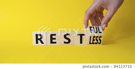 Restful and Restless symbol. Businessman hand turnes wooden cubes and changes word Restless to Restful. Beautiful yellow background. Business concept. Copy space Restful and Restless symbol. Businessman hand turnes wooden cubes and changes word Restless to Restful. Beautiful yellow background. Business concept. Copy space 94123710