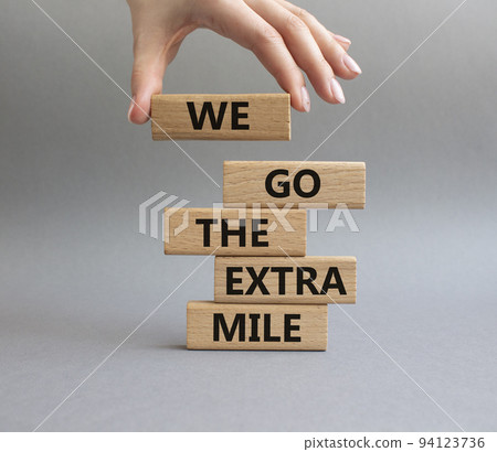 We go the extra mile symbol. Wooden blocks with words 'We go the extra mile'. Beautiful grey background. Businessman hand. Business and 'We go the extra mile' concept. Copy space. 94123736