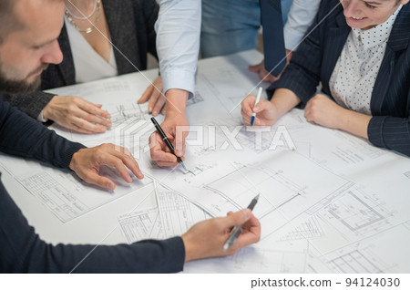Close-up of the hands of four colleagues with blueprints on the table in the office. Brainstorming of engineers and architects. Close-up of the hands of four colleagues with blueprints on the table in the office. Brainstorming of engineers and architects. 94124030