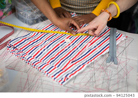With his finger, he points to a button that lies on the fabric. Tailor's workshop. With his finger, he points to a button that lies on the fabric. Tailor's workshop. 94125043