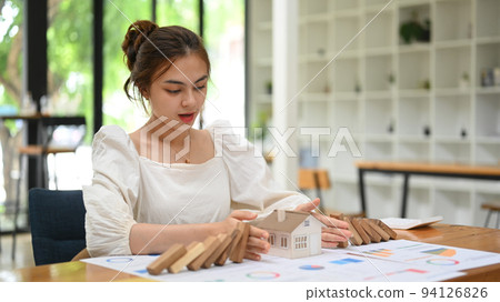 Woman protecting house model from falling wooden blocks. Home insurance, risk and problem concept Woman protecting house model from falling wooden blocks. Home insurance, risk and problem concept 94126826