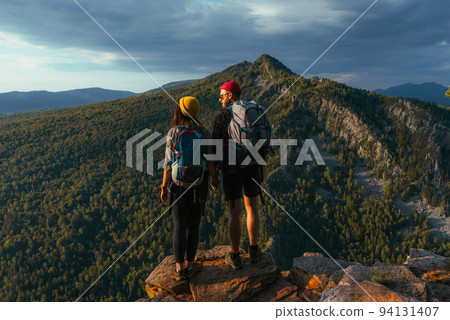 Travelers on the background of autumn mountains. Mountain tourism. Walking tour of the autumn mountains. A trip to the mountains with a backpack. A couple in love against the background of mountains Travelers on the background of autumn mountains. Mountain tourism. Walking tour of the autumn mountains. A trip to the mountains with a backpack. A couple in love against the background of mountains 94131407