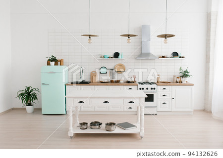 The bright Scandinavian-style kitchen features a mint-colored refrigerator. Wooden kitchen table with dishes The bright Scandinavian-style kitchen features a mint-colored refrigerator. Wooden kitchen table with dishes 94132626
