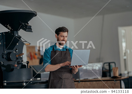 Business owner of small coffee factory working laptop on background of coffee roast machine Business owner of small coffee factory working laptop on background of coffee roast machine 94133118