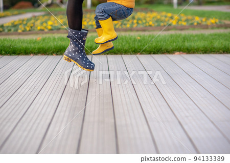 Feet in yellow rubber boots of a mother and son. Seasonality, seasons, fallen dry maple leaves 94133389