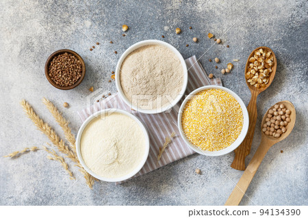 Food and baking gluten free ingredient. Cereals and flours coarse, corn flour, buckwheat flour, chickpeas flour over gray stone background. View from above. 94134390