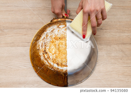 Woman's hand polishing half of a burnt frying pan Woman's hand polishing half of a burnt frying pan 94135080
