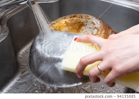Woman's hand polishing half of a burnt frying pan Woman's hand polishing half of a burnt frying pan 94135085