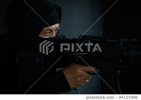 Side view of terrorist in black balaclava mask aiming with machine gun Side view of terrorist in black balaclava mask aiming with machine gun 94135406