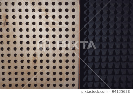 Wooden surface with round holes and black soundproof wall with acoustic dampening foam. Texture, pattern, background. 94135628