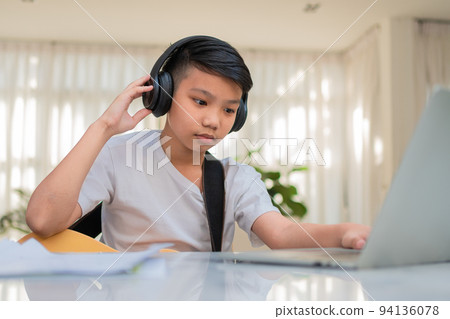 Asian boy playing guitar and watching online course on laptop while practicing for learning music or musical instrument online at home. Boy students study online with video call teachers play guitar. 94136078