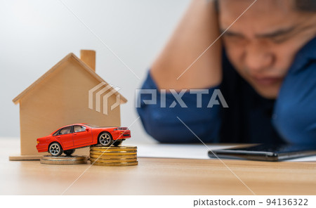 Unhappy Asian man holding a banknote and Making an account of income and expenses to pay the home loan and car loan, Concept loan payment and home insurance, economic problems, and inflation 94136322
