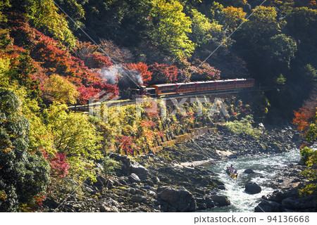 The Sagano Sagano Scenic Train running through Hozukyo Gorge in autumn and boats on the Hozugawa River 94136668