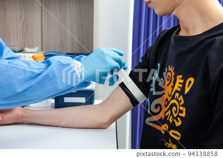 Nurse tightening the elastic band on a male patient arm to collect a blood sample from in a clinic Nurse tightening the elastic band on a male patient arm to collect a blood sample from in a clinic 94138858