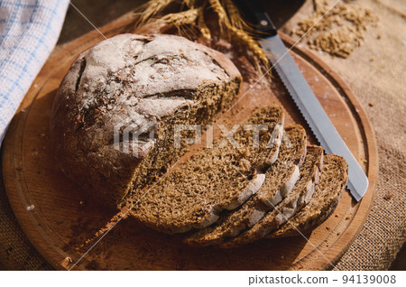 Top view slices of fresh baked sourdough bread on table with a burlap tablecloth, wheat ears and scattered cereal grains 94139008