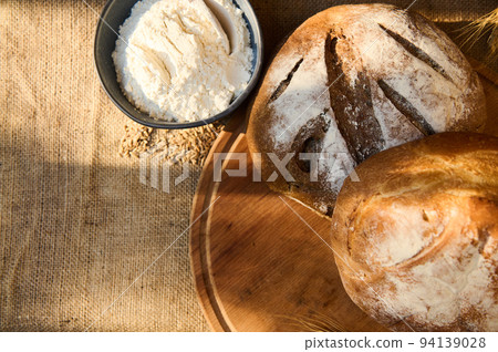 Loaves of fresh baked homemade whole grain and multigrain bread, on a wooden board with wheat spikelets, and white flour 94139028