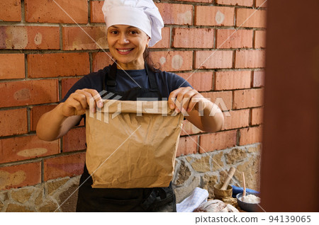 Beautiful woman, bakery shop worker holding a paper bag with packed fresh traditional bread and cute smiles at camera 94139065