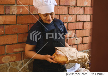 Close-up of a baker merchant packing a traditional sourdough bread into an eco paper bag in the artisanal bakery shop 94139066