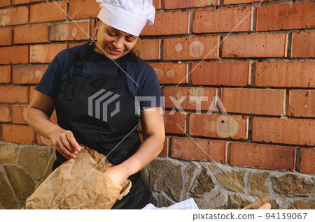 Portrait of a baker merchant packing a traditional sourdough bread into an eco paper bag in the artisanal bakery shop 94139067