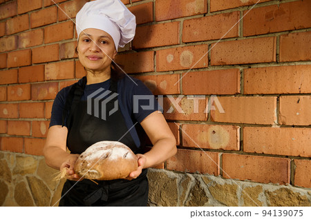 Happy woman baker entrepreneur holds loaf of bread, working at her artisanal family bakery store, selling homemade bread Happy woman baker entrepreneur holds loaf of bread, working at her artisanal family bakery store, selling homemade bread 94139075