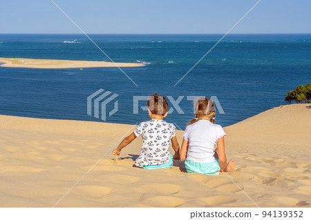 Girl and boy sitting on a huge sand dune, famous tourist destination Dune Pyla. Pilat Dune in France.  94139352