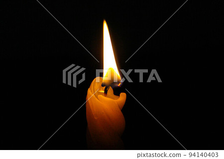 The candle burns in the dark. A yellow wax candle burns with a bright flame in absolute darkness. Close-up. Fire in the night. Religion and prayer. Religious ceremony in the church. Spiritual session The candle burns in the dark. A yellow wax candle burns with a bright flame in absolute darkness. Close-up. Fire in the night. Religion and prayer. Religious ceremony in the church. Spiritual session 94140403