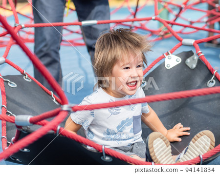 Laughing toddler is jumping on playground. Outdoor sport equipment for children physical development. Summer fun. 94141834